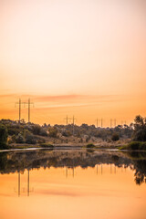 Fototapeta premium a calm lake with hills dotted with power poles in the background and an orange sunset sky in the background