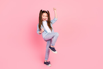 Full size photo of overjoyed small girl with ponytails dressed denim shirt raising fists up scream yeah isolated on pink color background