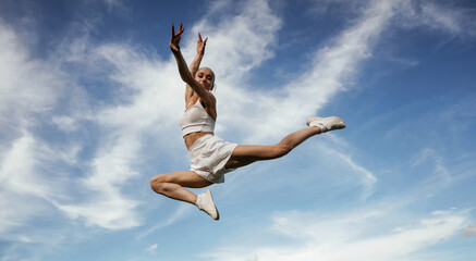 Blue sky with clouds, jumping. Young skinny fitness woman is outdoors