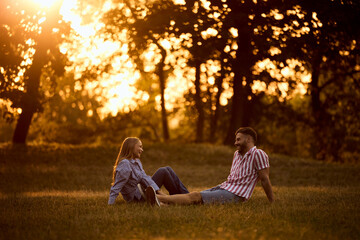 Two lovers laughing, enjoying the sunrise, sitting on the grass.