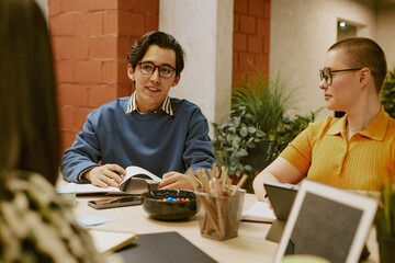 Young biracial man wearing eyeglasses telling about survey results during meeting with marketing team in modern office