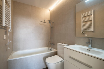 A contemporary bathroom featuring a bathtub with a shower fixture, a close-coupled toilet, a sleek sink with a faucet, and an illuminated wall mirror providing a clean ambiance.