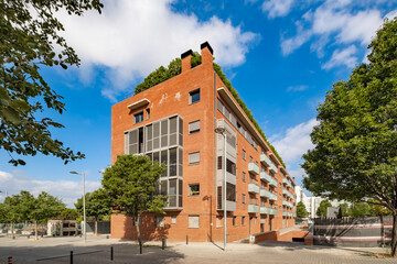 A large multi-storey apartment complex is depicted, featuring numerous balconies surrounded by trees and clear skies, indicating a spacious and well-designed urban living space.