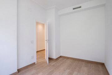 Fototapeta premium An empty room featuring clean white walls and polished wooden flooring, with an open door leading to an adjacent, softly lit space, ideal for new beginnings.