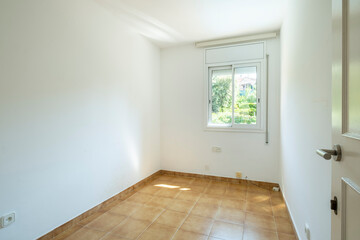 A compact, bright room featuring a sizable window allowing abundant natural light, adorned with tiles on the floor, presenting a peaceful and inviting atmosphere.