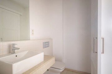 A clean, modern bathroom with white walls, minimalistic design, featuring a sink, countertop, wall-mounted fixtures, and a simple yet modern aesthetic.