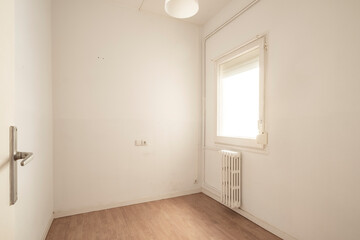 A smaller room featuring a single window with a radiator beneath it, plain white walls, and minimalistic design creating a simple and clean atmosphere.