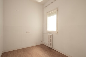 Small room featuring a single window letting in bright natural light, a radiator beneath the window, and white walls, offering a simplistic and clean environment.