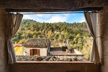 Through a rustic, open window with curtains, there's a breathtaking view of green hills and trees, capturing the essence of tranquility and natural beauty.