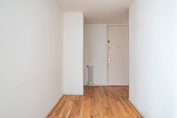 Empty minimalist hallway featuring white walls and wooden flooring with a small radiator near the entrance, casting a simple and clean modern aesthetic.