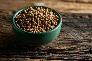 Close-up of Raw Organic Coriander Seeds in a Green Bowl on Old Wood Background with Text Space