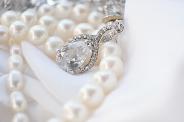 A beautiful pearl necklace with a diamond-studded pendant is displayed on white fabric. The photo emphasizes the sophisticated design and luxurious appeal of premium jewelry.