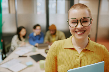 Medium closeup of cheerful young stylish female office worker with buzz haircut standing in board room and smiling at camera