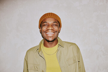 Medium closeup portrait of cheerful young African American man wearing beanie smiling at camera