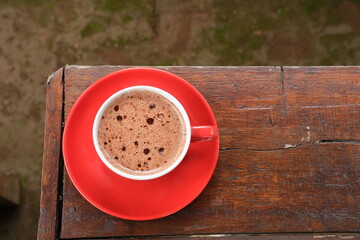 A top view of a steaming cup of hot chocolate in a vibrant red cup and saucer on a rustic wooden...