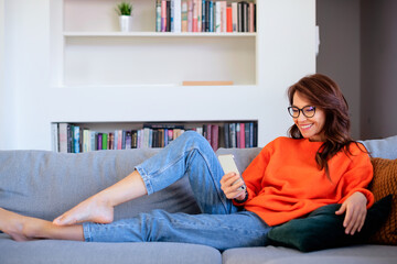Full length of a mid aged woman relaxing at home and using a smartphone