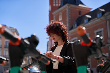Young happy woman renting scooter using mobile app in smartphone, modern transport in big city
