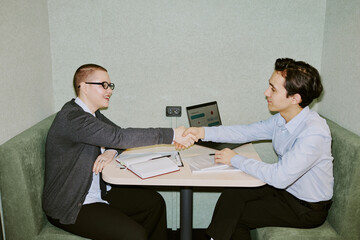 Flash shot of two male and female coworkers sitting in front of each other in modern office doing handshake