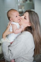 Mom holding and kisses newborn baby  in room at home. Motherhood. 
