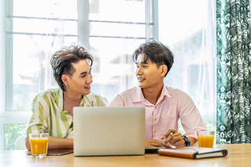 Asian businessman gay work with smile and laugh in office. Attractive male lgbtq collegues working together with using laptop pc and paper showing graphic chart in living room, Lgbt love concept