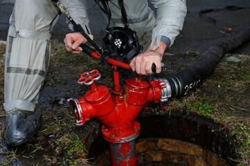 Rescuer hands in protective rubber costume turning valve of fire hydrant to water plant territory