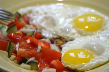 Fried eggs with tomato, cucumber and onion on a plate