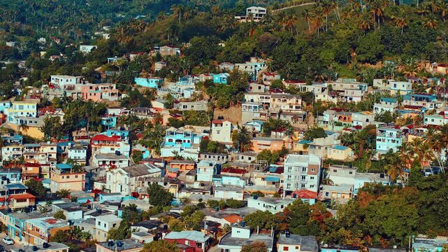 Picturesque panoramic view of a provincial cityscape with hills and mountain peaks in the background. Summer evening in the Dominican mountains. Bright walls of houses among tropical nature.