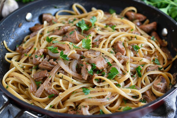 A pan filled with linguine pasta, cooked chicken liver, sautéed onions, and garnished with fresh parsley