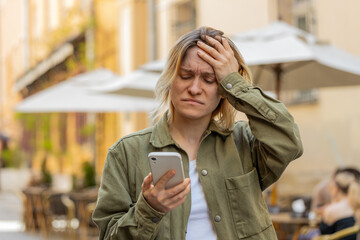 Caucasian young woman using smartphone typing browsing loses becoming surprised sudden lottery...