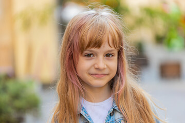 Portrait of happy preteen child kid smiling friendly, glad expression looking at camera dreaming, resting, relaxation feel satisfied good news. Pretty blonde school girl on city urban street, outdoors