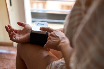  Mid adult woman checking her blood pressure at home. Hispanic Woman Measuring Blood Pressure at Home Using Digital Monitor for Healthcare and Wellness.