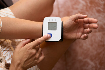  Mid adult woman checking her blood pressure at home. Hispanic Woman Measuring Blood Pressure at Home Using Digital Monitor for Healthcare and Wellness.