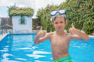 Happy young boy relaxing on the side of a swimming pool wearing goggles with thumbs up © Danko