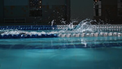 Side view tracking slowmo shot of determined male athlete with arm tattoo using freestyle stroke technique while swimming race in indoor pool