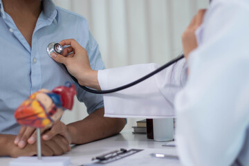 A beautiful Asian female doctor is measuring a patient's blood pressure and listening to his heartbeat. Ayoung man who came to see a doctor at a hospital.
