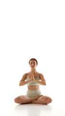 Woman in athletic wear sits in cross-legged position, eyes closed, hands in prayer pose, exuding calm, embodying meditation and inner peace. Concept of beauty, mindfulness and balance, concentration.