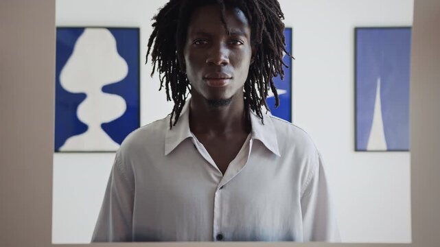 Young Black man examining artworks with interest while visiting exhibition of modern art in gallery