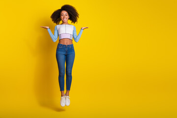 Full length photo of lovely young lady jump compare empty space dressed stylish blue garment isolated on yellow color background