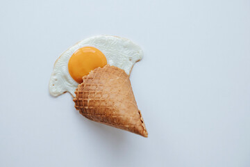 Scrambled eggs with waffle cone imitate melted ice cream on light background