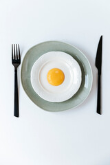 plates stacked one on top of another with imitation scrambled eggs, a raw yolk in the center. black cutlery nearby