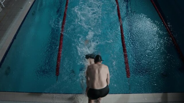 High angle slowmo shot of two professional male swimmers having relay race in indoor pool with lanes