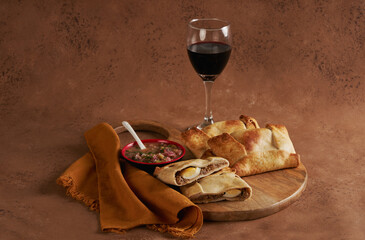 Bodegón Empanadas de Pino, pebre y copa de vino sobre una tabla de cocina de madera