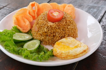 Nasi goreng- Indonesian fried rice with fried egg,frsh vegetable and kerupuk crackers in plate on wooden table . Indonesian Food