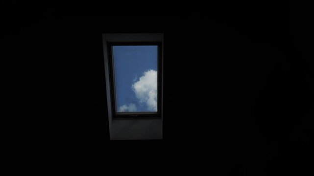 View from a dark room through a skylight or window to a blue sky and fluffy white clouds. Accelerated time-lapse video of clouds moving across the sky on a sunny day.
