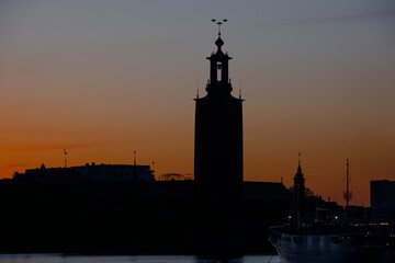 Panoramic view of Stockholm City hall at sunset with orange sky and calm water reflection. Scenic skyline of the Swedish capital at dusk. 