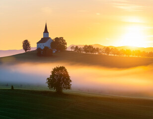 Obraz premium A serene sunrise landscape with a church on a hill surrounded by mist