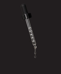 A drop of cosmetic oil falls from the pipette on black background