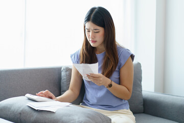 Asian woman holding paper document calculating money savings paying bills in mobile application using smart phone payment online with paying household bills tax insurance managing budget.