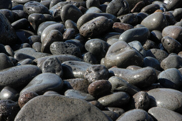 Close-up of black volcanic stones on a Funchal, Madeira beach, showcasing their unique texture and color in the coastal environment.