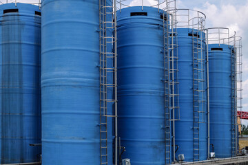 Blue vertical liquid chemical storage tanks with ladders. Close-up.